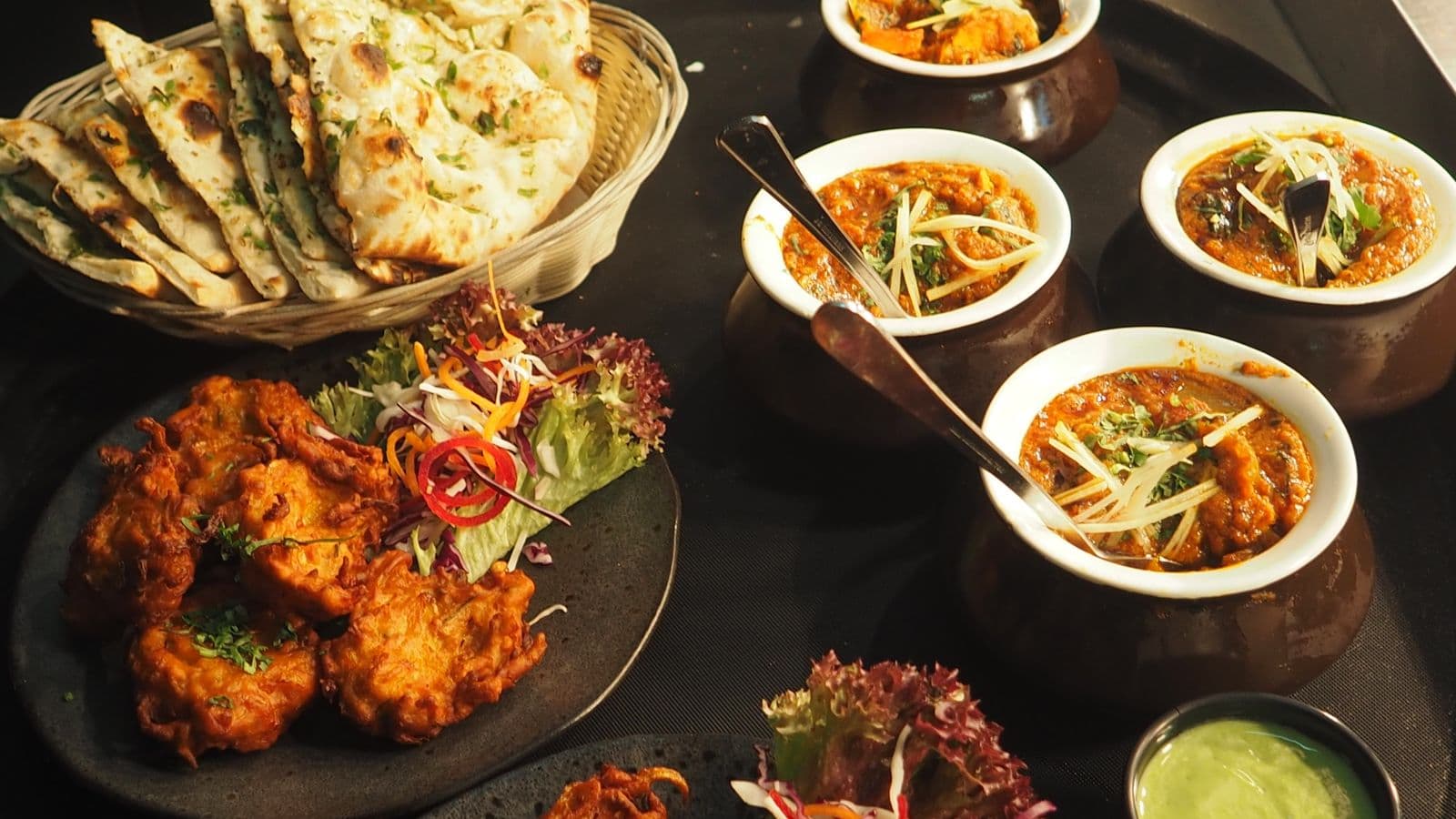 A shared table of warm dishes — naan, curries, and sides ready to be passed around